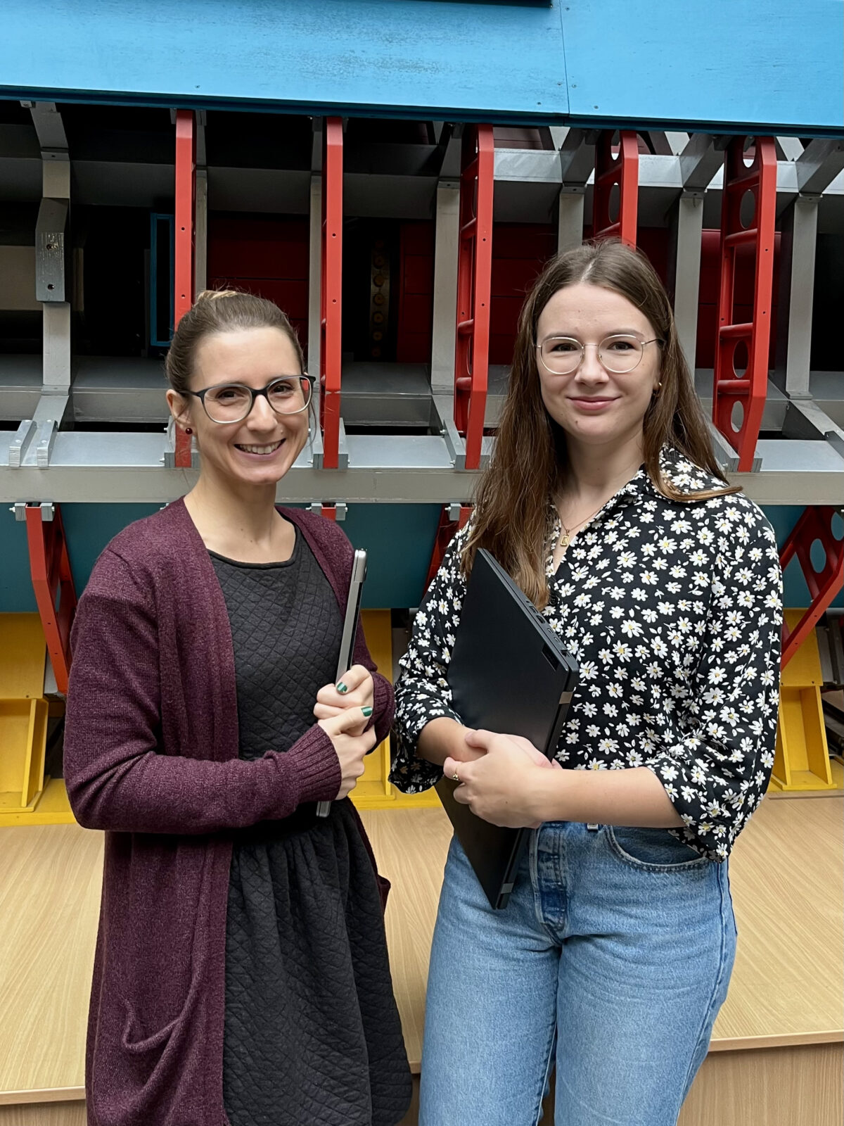 Zwei Frauen mit Laptops unterm Arm stehen vor einem Detektormodell